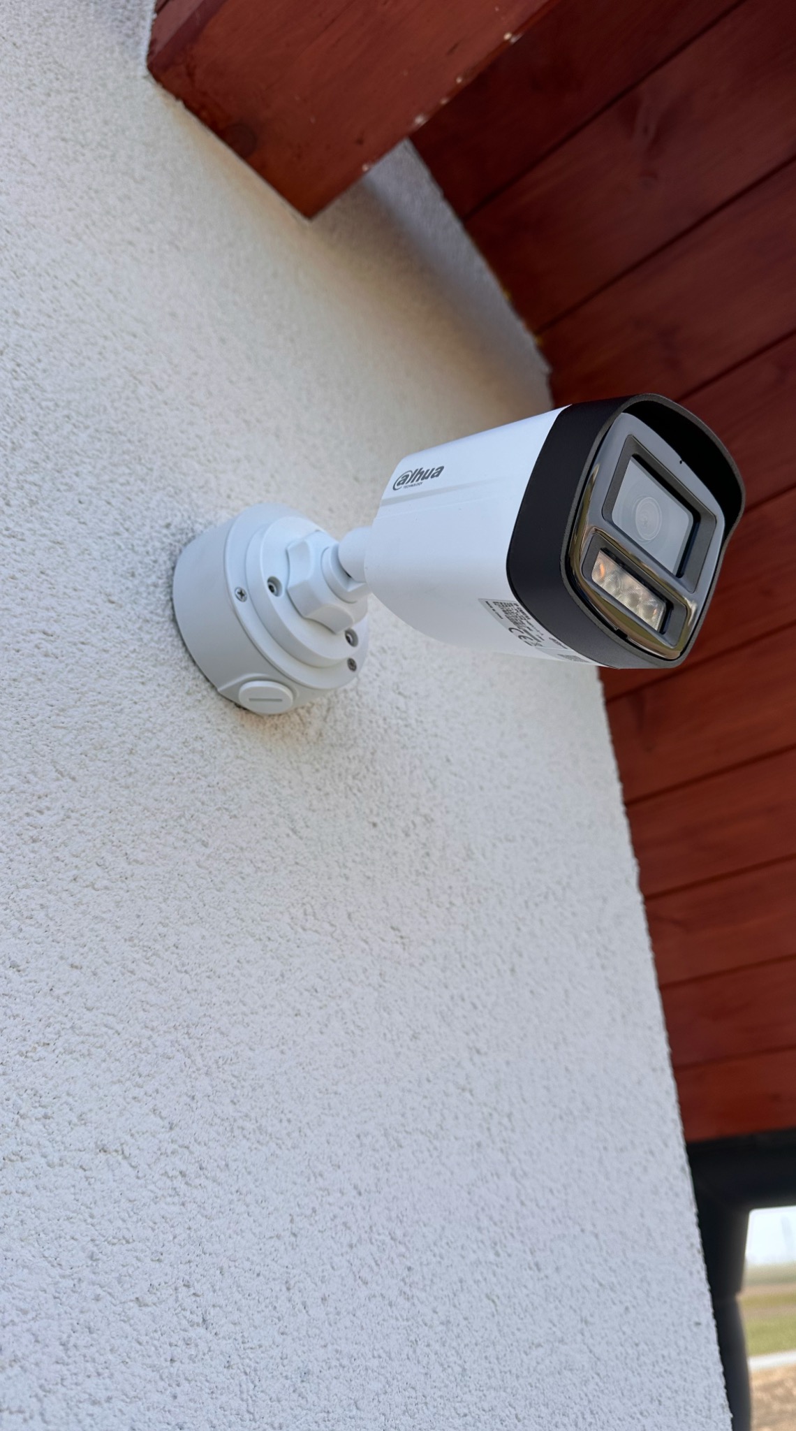 Kamera przemysłowa Dahua zamontowana na jasnej, chropowatej ścianie budynku z elementami drewnianej konstrukcji dachu widocznymi w tle.
