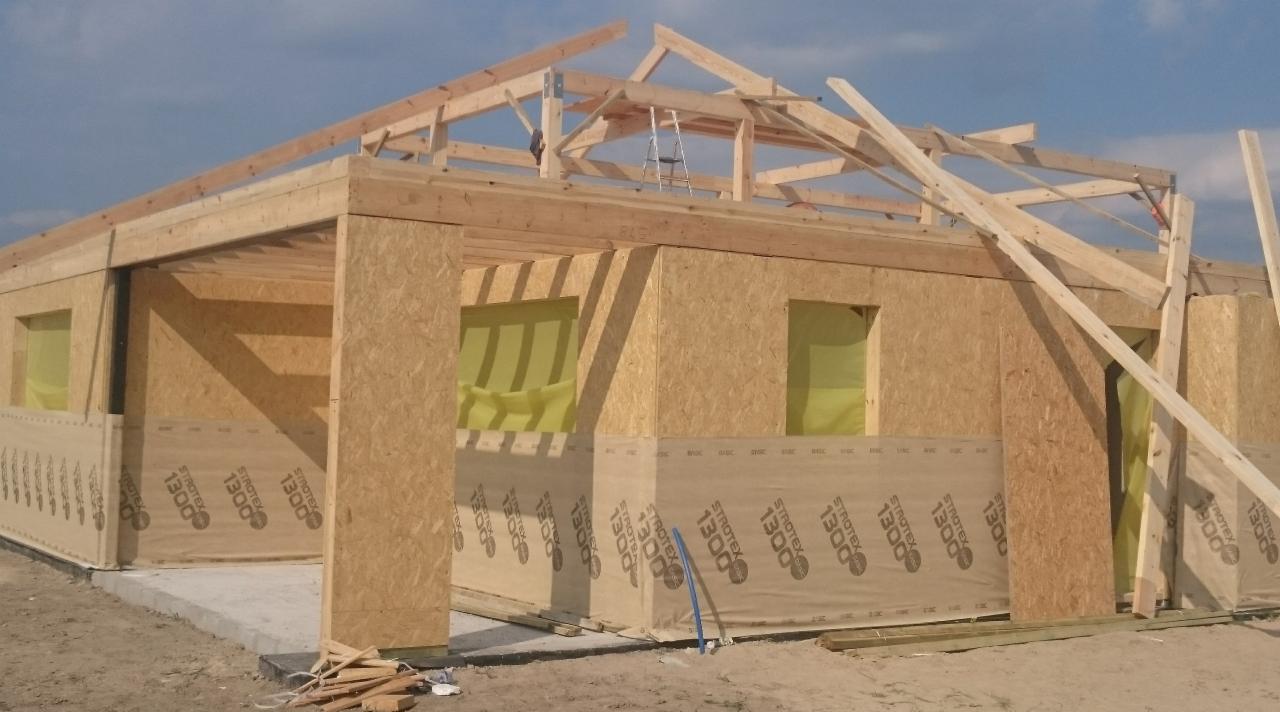 Budowa parterowego domu w technologii szkieletowej, widoczne ściany z płyt OSB i drewniana konstrukcja dachu w trakcie montażu, drabina oparta o krokwie.