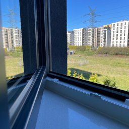 Amadin Cleaning Solution Oleksii Zazymko - Otwarty fragment okna z widokiem na osiedle mieszkaniowe, trawnik i słup wysokiego napięcia w słoneczny dzień.