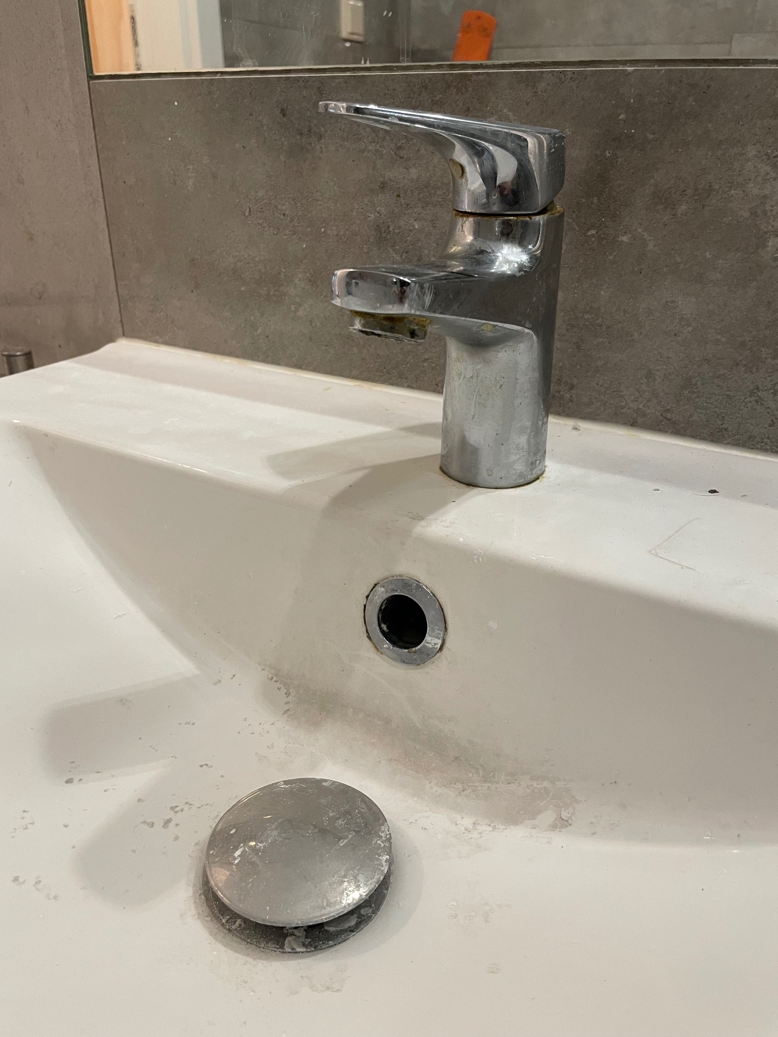 Zabrudzona, biała umywalka z chromowaną baterią, pokryta osadem i plamami, z widocznym korkiem spustowym obok odpływu.