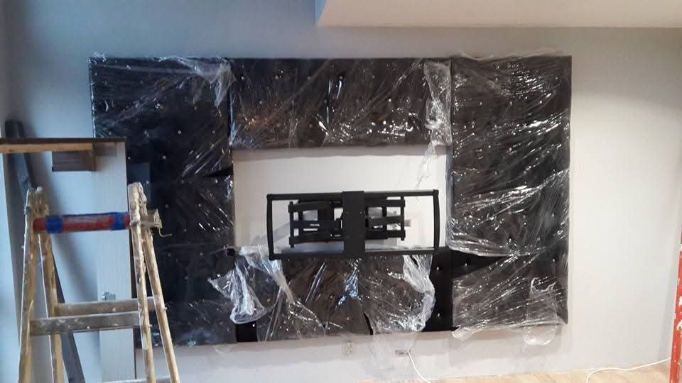 Przygotowanie do montażu telewizora: panel dekoracyjny obity materiałem zabezpieczony folią, na ścianie zamontowany uchwyt, obok drabina malarska.