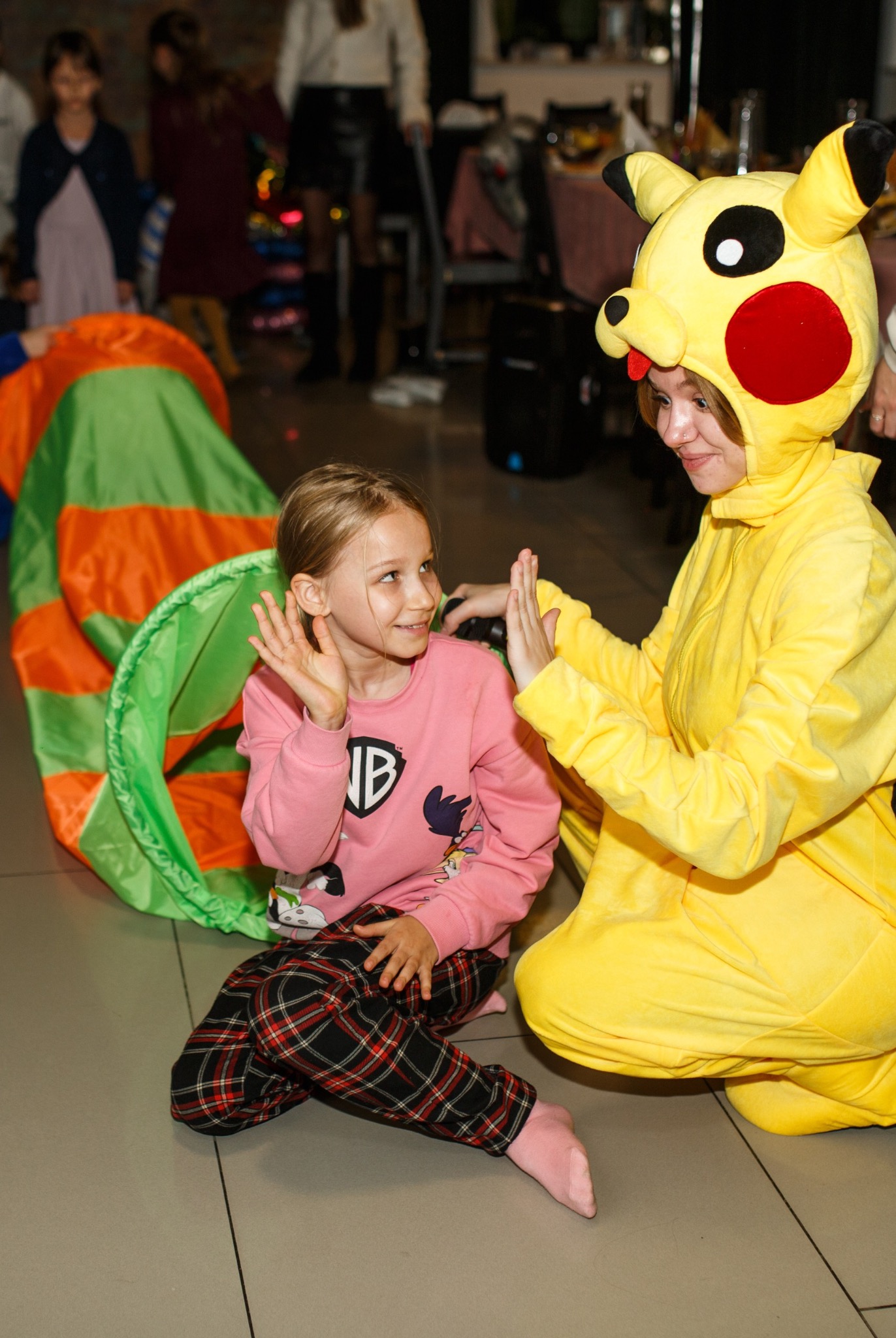 Animator w stroju Pikachu bawi się z dziewczynką przy tunelu animacyjnym. Radosna interakcja, uśmiech dziecka i kostium tworzą żywą, eventową atmosferę.