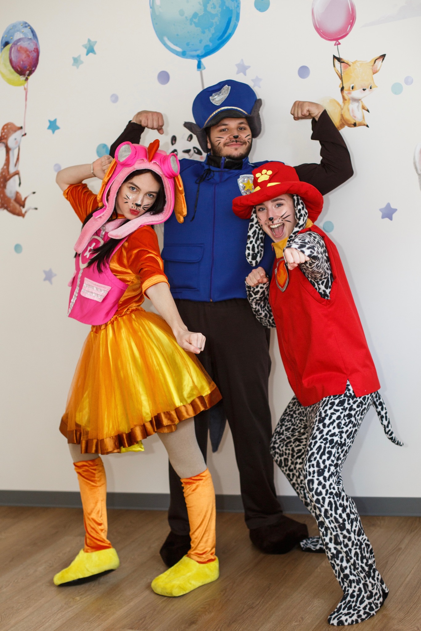 Animatorzy przebrani za postacie z bajki 'Psi Patrol', w kostiumach Skye, Chase i Marshall, pozują na tle ściany z motywem balonów i gwiazd.