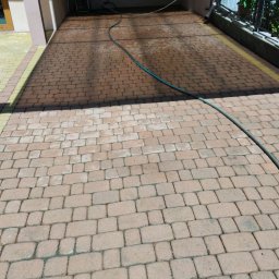 Mateusz Buczek - Częściowo umyta kostka brukowa na podjeździe z widocznym wężem ogrodowym i różnicą w kolorze między czystą a brudną powierzchnią.