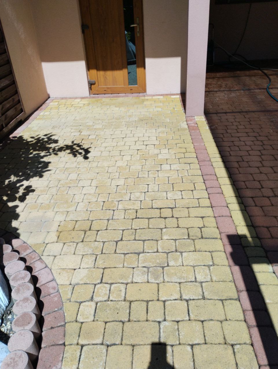 Żółta kostka brukowa po czyszczeniu, przylegająca do wejścia z brązowymi drzwiami, z widocznymi śladami cienia drzewa.