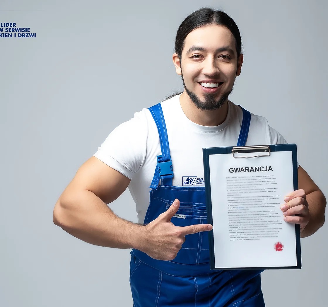 Uśmiechnięty monter w niebieskim kombinezonie, wskazujący na dokument gwarancyjny z pieczęcią, logo firmy widoczne na kombinezonie.