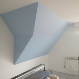 Usługi ogulnobudowlane - Pomalowane na błękitno skośne poddasze z widoczną przecinarką do płytek i grzejnikiem.