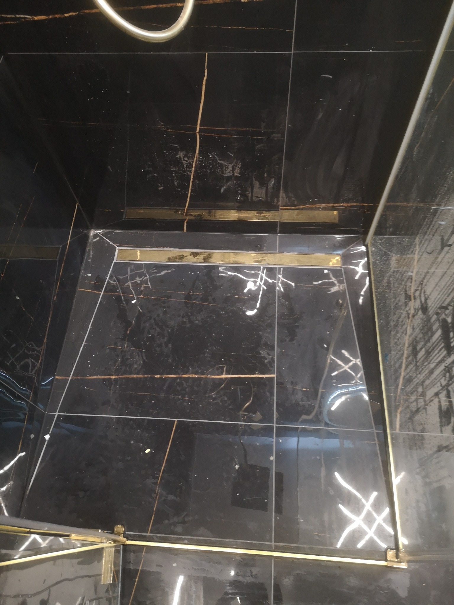 Czarna, marmurkowa posadzka kabiny prysznicowej z odpływem liniowym w złotym kolorze, widoczne ślady po czyszczeniu.