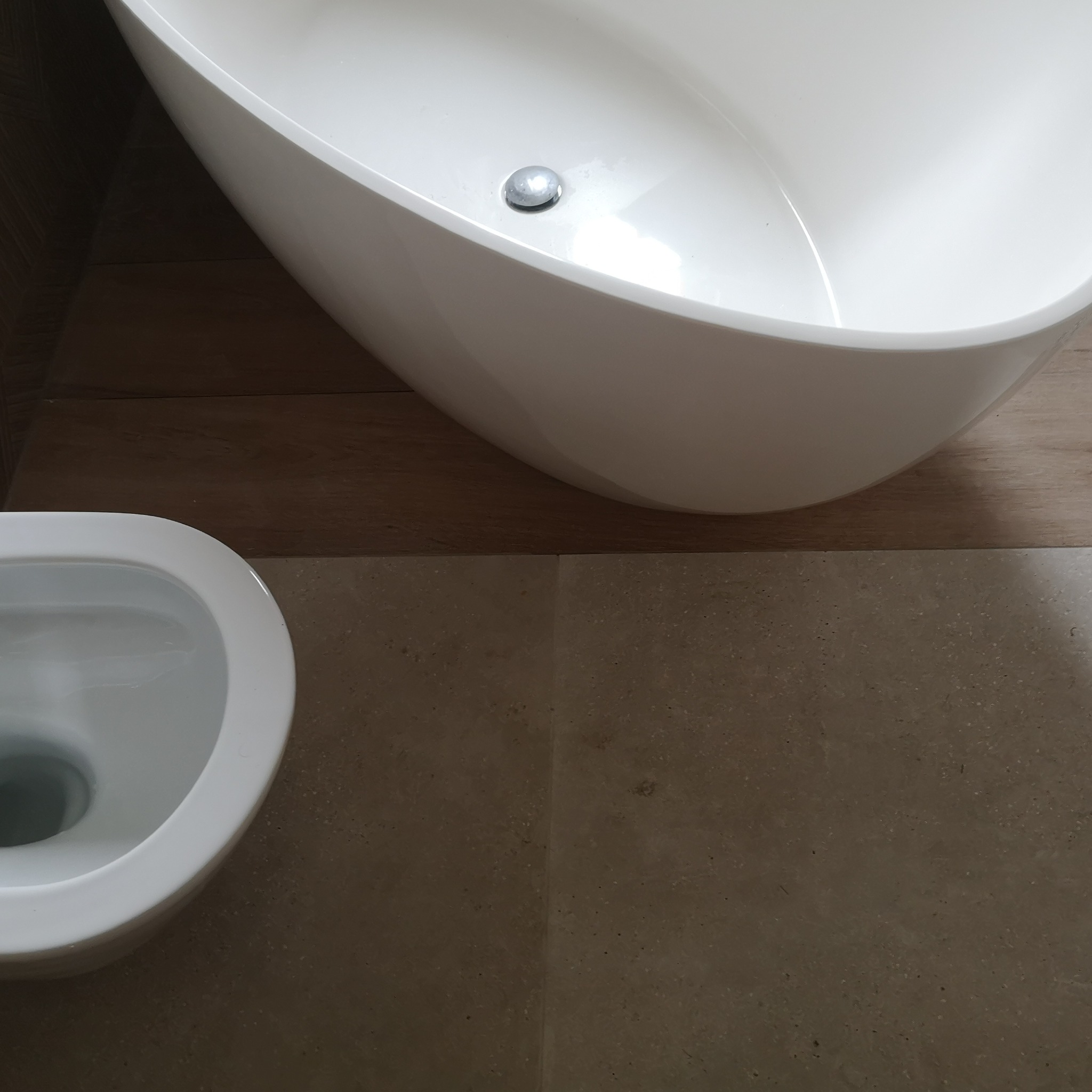 Minimalistyczna łazienka w Kasince Małej z wolnostojącą białą wanną i toaletą, wykończona płytkami w odcieniach beżu i brązu.