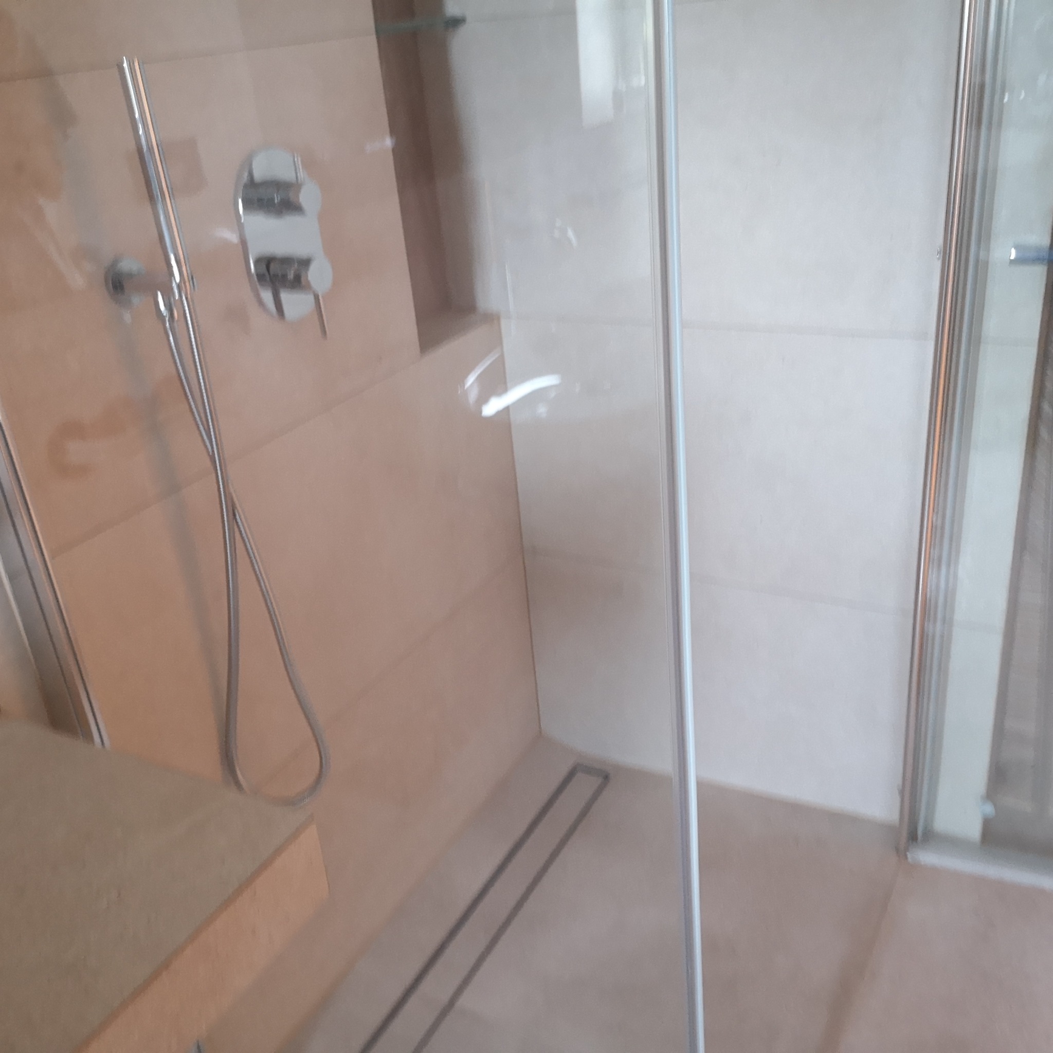 Nowoczesny prysznic walk-in z odpływem liniowym, wykończony beżowymi płytkami, chromowana armatura.