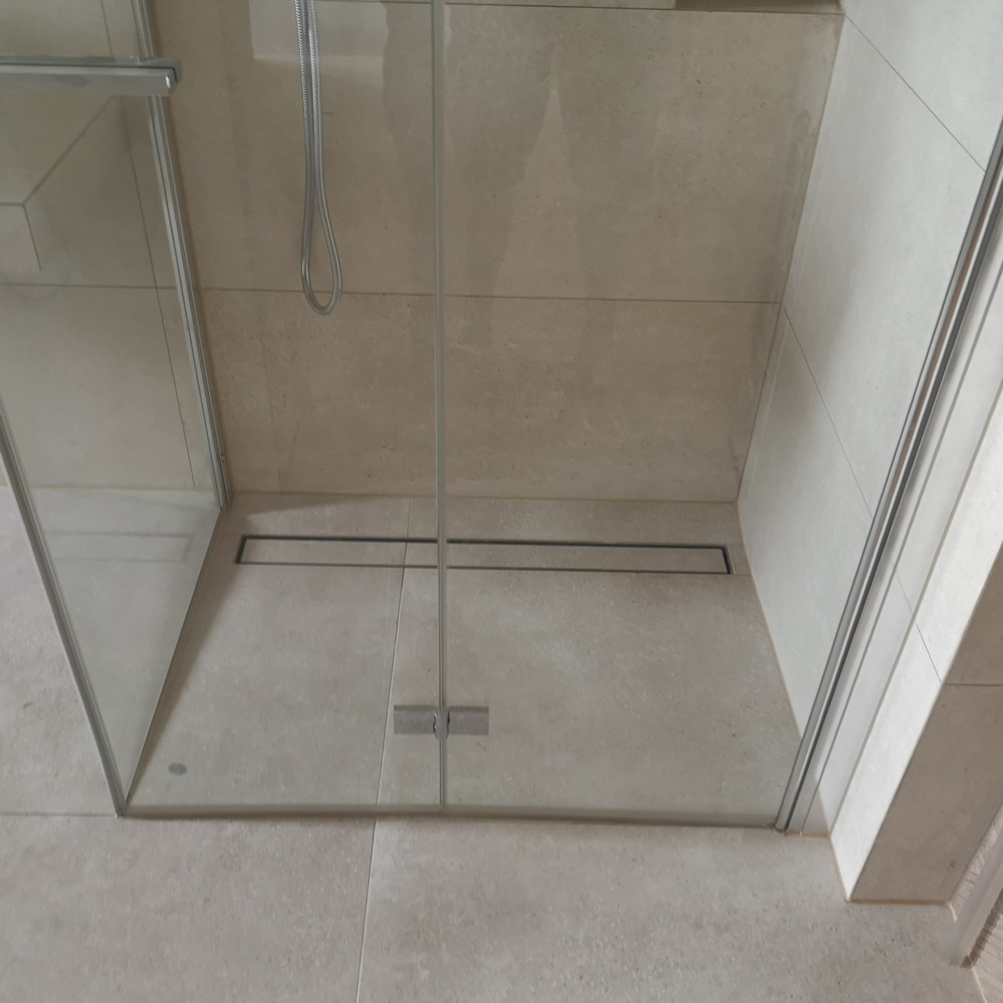 Kabina prysznicowa z odpływem liniowym w posadzce wyłożonej beżowymi płytkami, widok z góry.