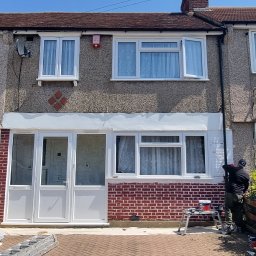 Filip Krzaczek - Malowanie elewacji szeregowego domu z ceglaną wstawką; widoczny pracownik na rusztowaniu i puszki z farbą.