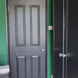 Filip Krzaczek - Pomalowane na szaro drzwi wewnętrzne z czterema panelami, na tle zielonej ściany i czarnej szafy z kryształowymi gałkami.