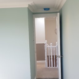 Filip Krzaczek - Świeżo wykończone wnętrze z pomalowanymi na pastelowy błękit ścianami, białym sufitem z zamontowanymi punktowymi lampami i białymi listwami przypodłogowymi. Widok na korytarz z szarą wykładziną...