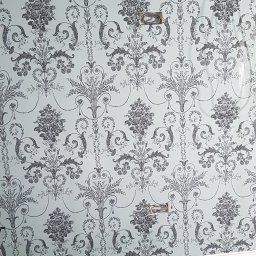 Filip Krzaczek - Ściana po położeniu jasnoniebieskiej tapety w ciemnoszary, kwiecisty wzór, widoczne puszki elektryczne, listwa przypodłogowa i fragment podłogi w trakcie remontu.