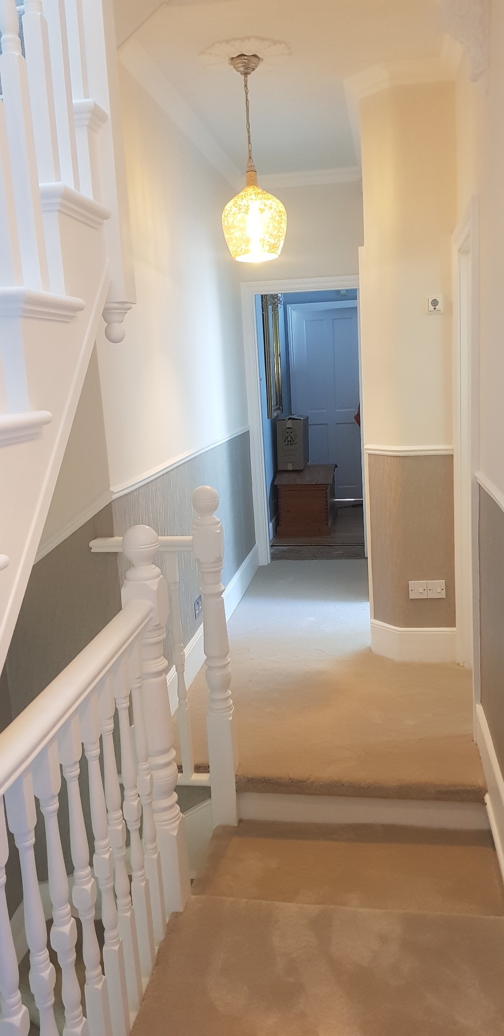 Odnowione wnętrze korytarza z pomalowanymi ścianami na biało i szaro, widoczne schody z białymi balustradami oraz ozdobna lampa wisząca.
