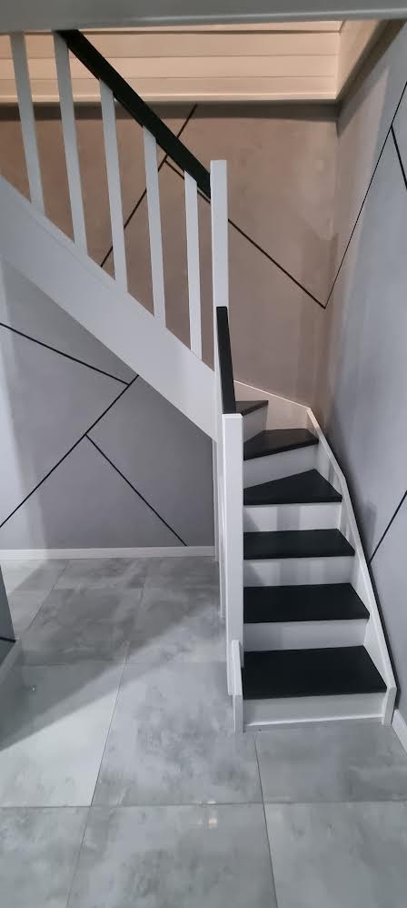 Schody wewnętrzne z białymi balustradami i czarnymi stopniami w Rumi, na tle ściany z geometrycznym wzorem.