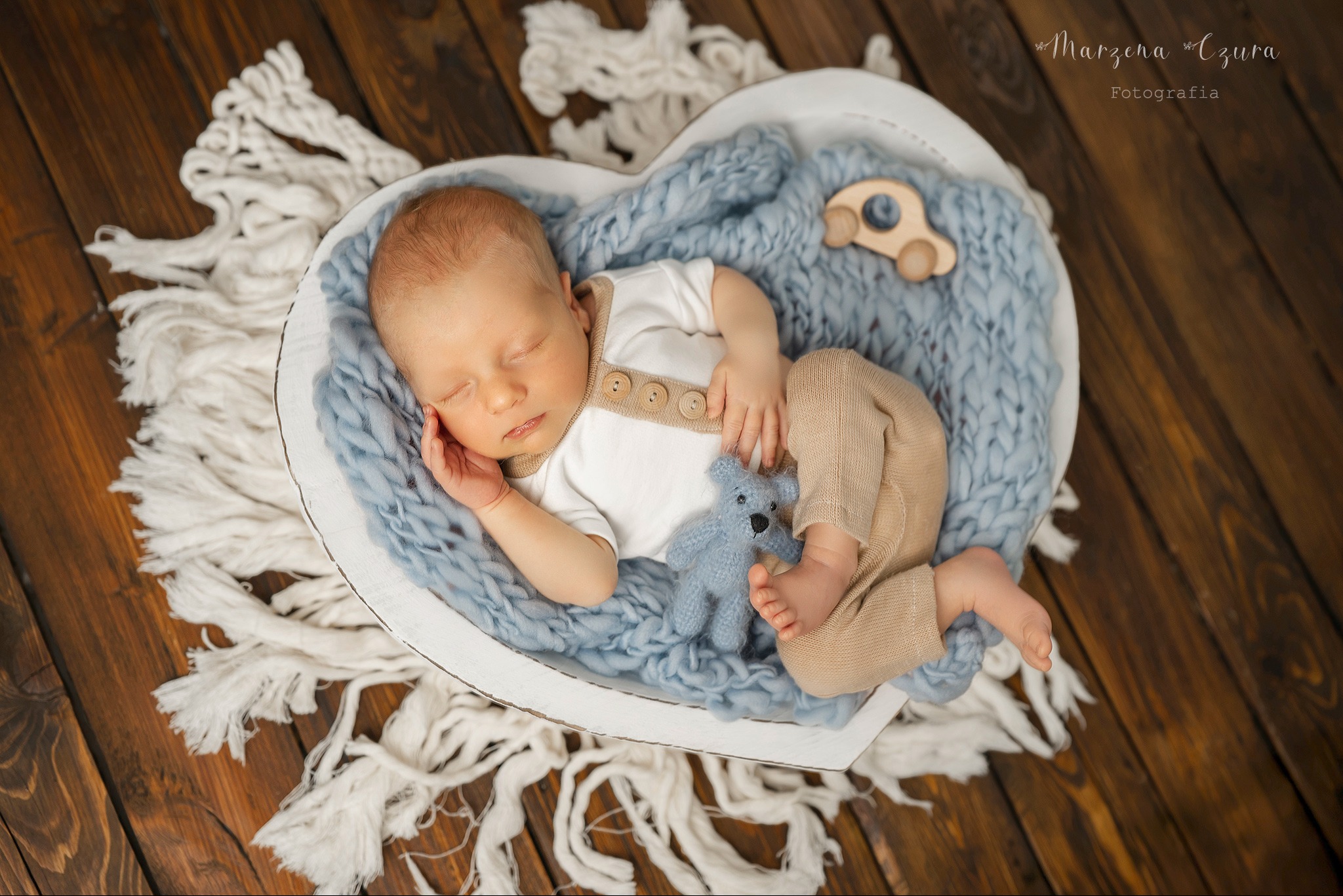 Słodki sen noworodka w sercu z dzianiny, Bochnia. Urocza sesja w studio: niemowlę śpi otulone miękkim kocykiem, z małym pluszowym misiem i drewnianą zabawką.