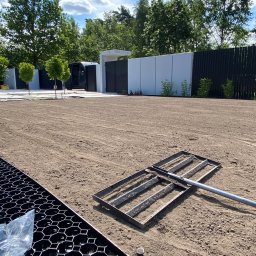 Szymon w Ogrodzie - Przygotowane podłoże pod trawnik z rolki, wyrównane grabiami. W tle małe drzewka, ogrodzenie z paneli i budynek gospodarczy. Elementy drenażowe w lewym dolnym rogu.