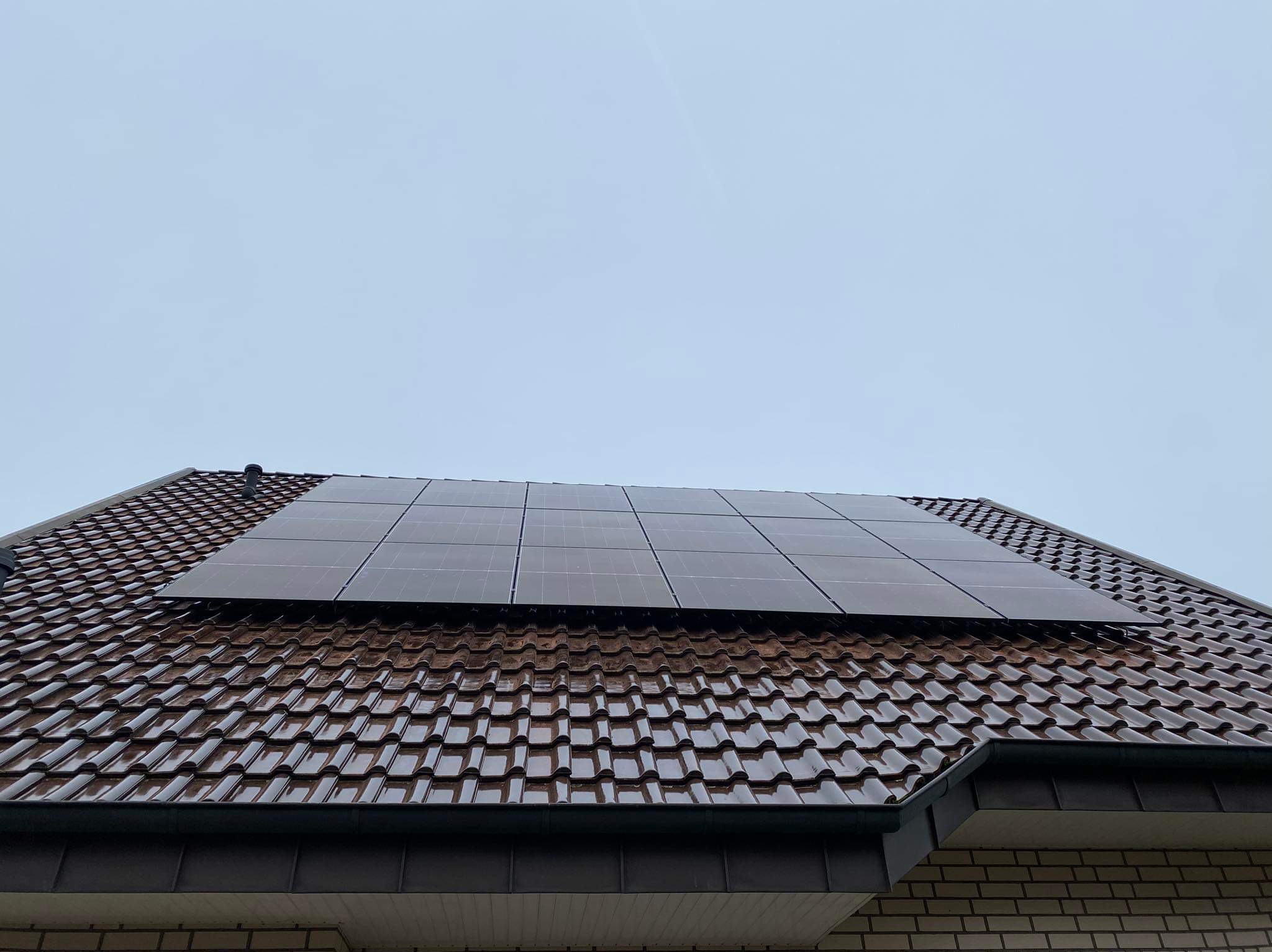 Panel słoneczny na brązowym, błyszczącym dachu ceramicznym w pochmurny dzień.