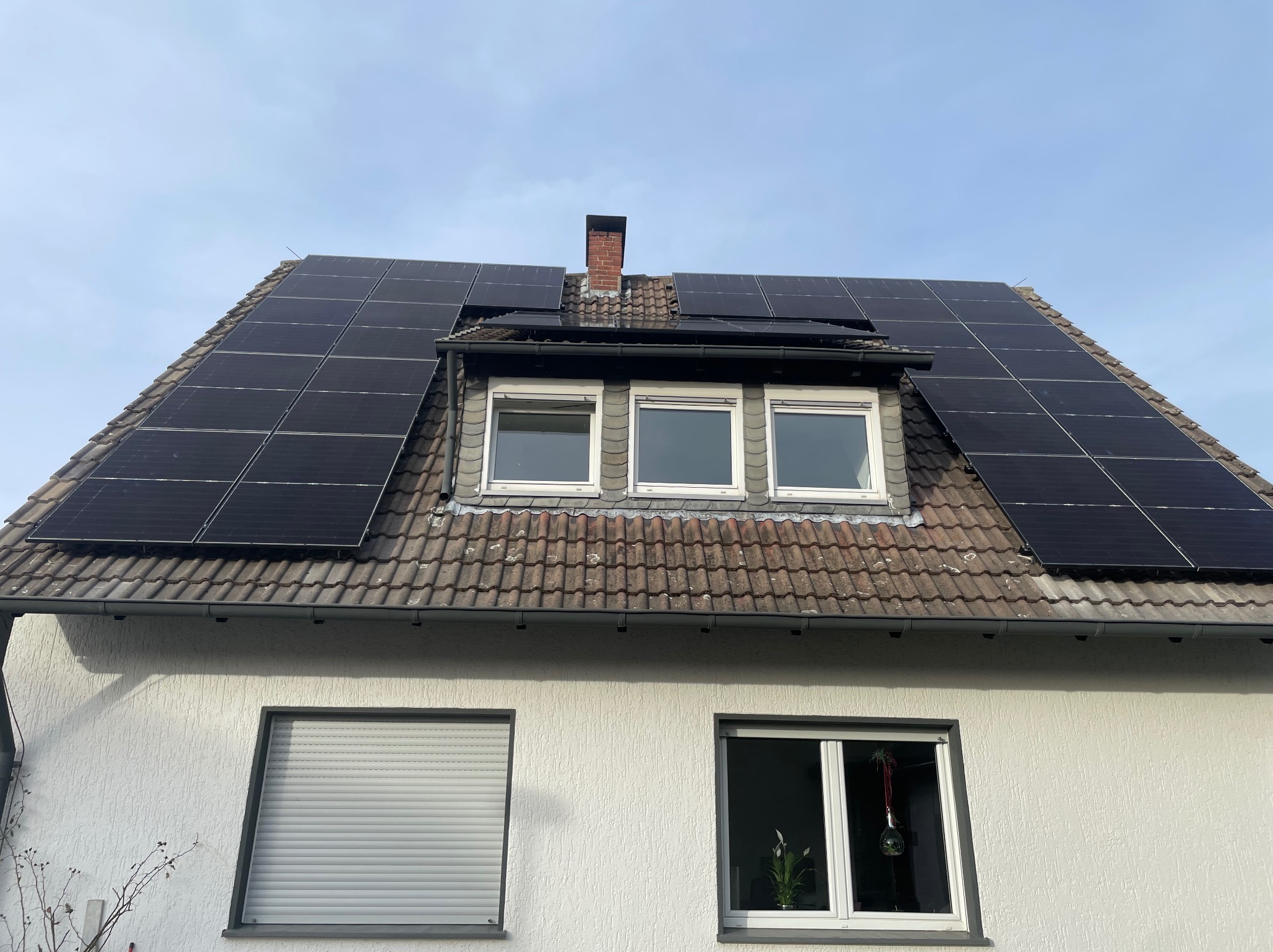 Dom z panelami słonecznymi na dachu pokrytym dachówką ceramiczną, widoczne okna dachowe i komin.
