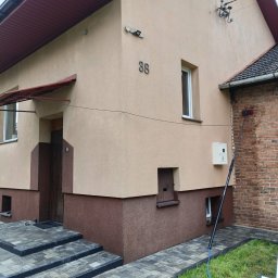 Royal Clean Sp. z o.o. - Dwukolorowa elewacja domu z numerem 38, brukowane schody i ścieżka. Długa tyczka z myjką i wężem oparta o mokrą ceglaną ścianę, sugerująca czyszczenie fasady.