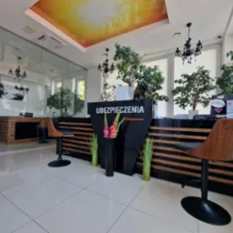 Nowoczesne biuro z recepcją z napisem 'Ubezpieczenia Optimum', drewnianymi krzesłami barowymi, roślinami doniczkowymi i podświetlanym sufitem.