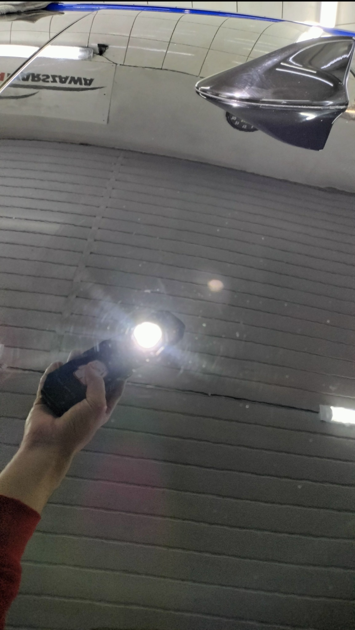 Lampa inspekcyjna w dłoni oświetla lakierowany dach samochodu z anteną typu płetwa rekina, uwidaczniając jego gładkość i brak defektów po polerowaniu.