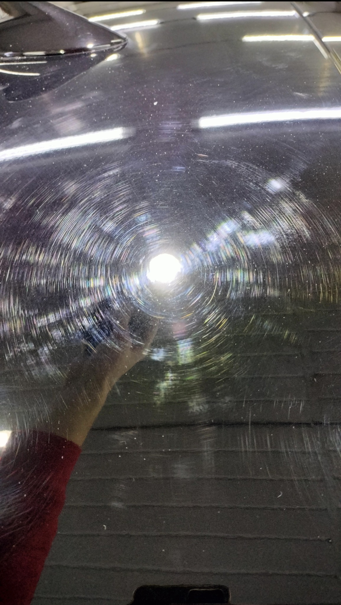 Polerowana, czarna powierzchnia z widocznymi kolistymi śladami po polerowaniu, odbijająca światło lampy i rękę osoby robiącej zdjęcie w tle.