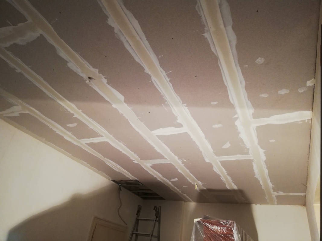 Sufit z płyt kartonowo-gipsowych w trakcie szpachlowania spoin, widoczny otwór rewizyjny i drabina w pomieszczeniu.