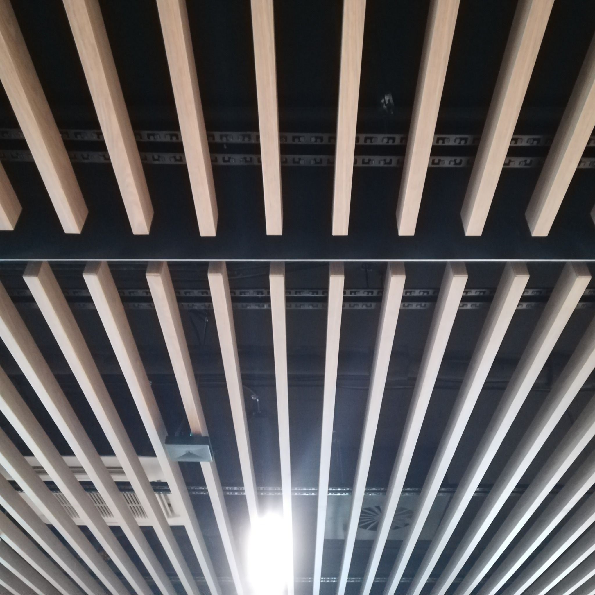 Drewniane lamele sufitowe ułożone równolegle, widoczne elementy oświetlenia i instalacji nad sufitem podwieszanym.