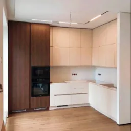 Nowoczesna kuchnia w Krakowie z białymi i drewnianymi szafkami, zintegrowanym piekarnikiem i mikrofalówką, oraz drewnianą podłogą. Oświetlenie sufitowe liniowe.