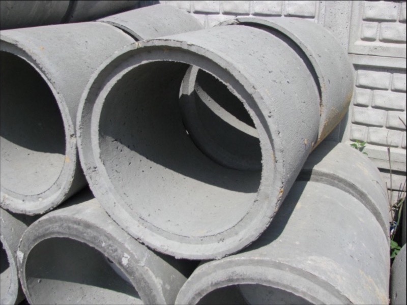 Stos szarych, betonowych rur o okrągłym przekroju, widoczna tekstura betonu i wnętrze rur, w tle fragment betonowego muru.