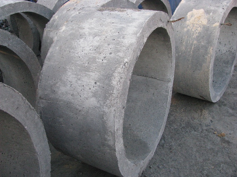 Betonowe kręgi studzienne ułożone jeden na drugim, widoczne surowe wykończenie betonu i ślady po szalunku.