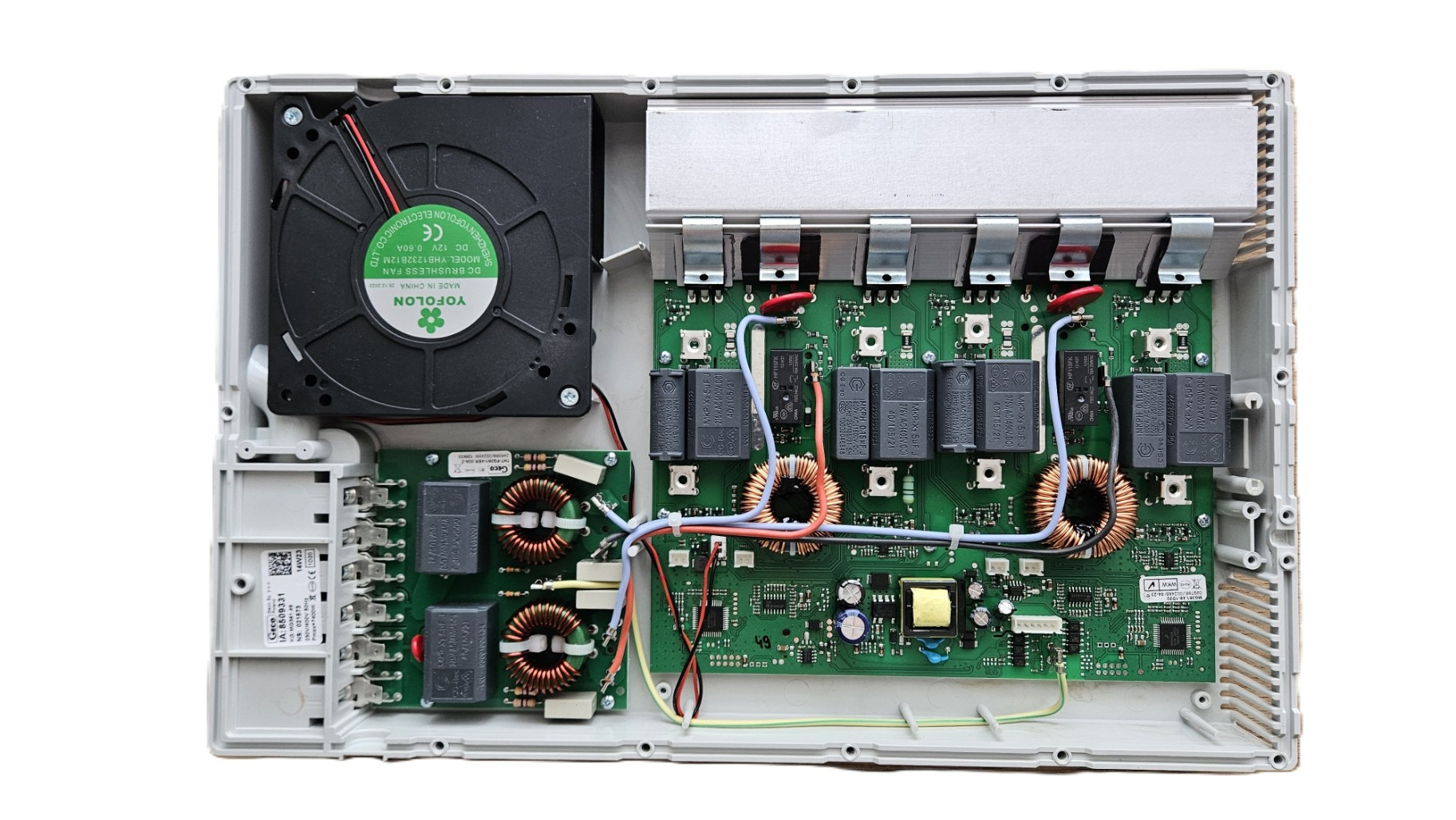 Wnętrze urządzenia elektronicznego z widoczną płytą główną, elementami elektronicznymi, wentylatorem i radiatorem. Detaliczne ujęcie elektroniki w szarej obudowie.
