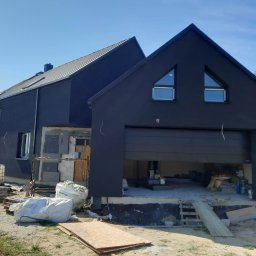 Usługi ogólnobudowlane Jakub Czech - Nowoczesny dom z ciemną elewacją w trakcie prac wykończeniowych, widoczne materiały budowlane i otwarty garaż.