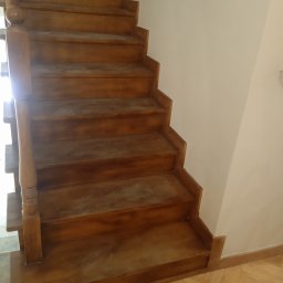 AS-BUD - Drewniane schody z balustradą, widoczne ślady szlifowania przed lakierowaniem, jasne ściany w tle.