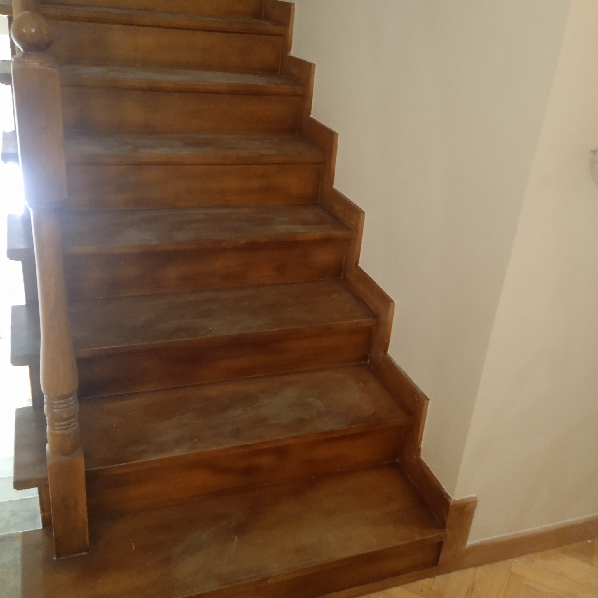 Drewniane schody z balustradą, widoczne ślady szlifowania przed lakierowaniem, jasne ściany w tle.