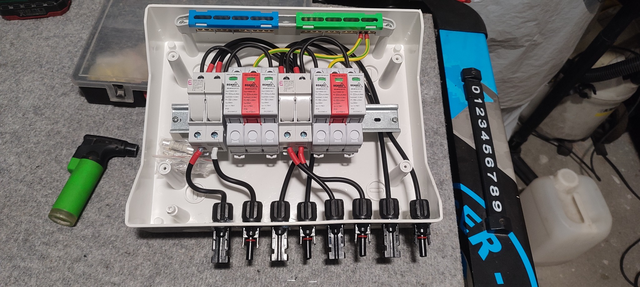Rozdzielnica elektryczna DC z zabezpieczeniami przepięciowymi Bemko, widoczne przewody zasilające, złączki MC4, listwy zaciskowe Wago i narzędzie do lutowania na szarym tle.