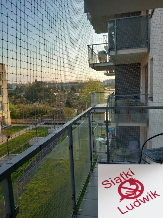 Zabezpieczenie balkonu siatką z drobnymi oczkami, widok na miasto w tle, w prawym dolnym rogu logo firmy.