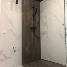 Nowoczesna kabina prysznicowa walk-in z czarną armaturą i panelami z drewna, wykończona płytkami imitującymi marmur.
