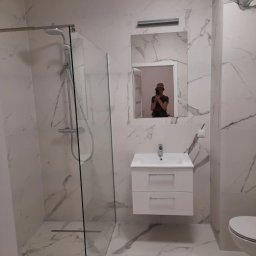 Rem & bud - Nowoczesna łazienka z kabiną prysznicową typu walk-in, białą szafką z umywalką i lustrem, wykończona płytkami imitującymi marmur, z widocznym odbiciem osoby robiącej zdjęcie w lustrze.