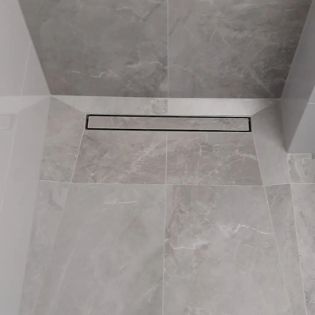 Szare płytki imitujące marmur w kabinie prysznicowej z odpływem liniowym, widok z góry.