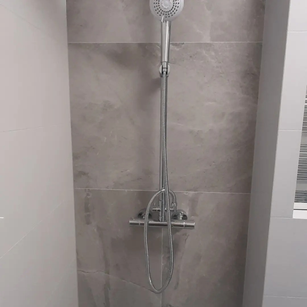 Nowoczesny prysznic z deszczownicą i baterią termostatyczną na ścianie wyłożonej szarymi płytkami imitującymi marmur, w jasnej łazience.