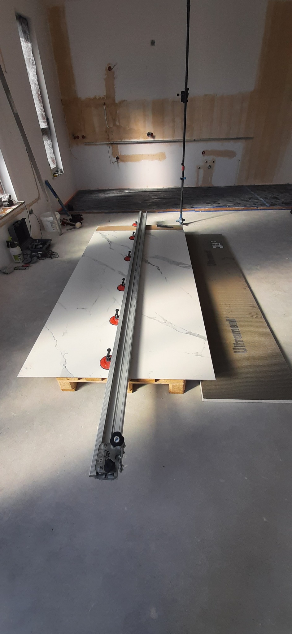 Przygotowanie do cięcia wielkoformatowej płyty gresowej z marmurowym wzorem, użycie przyssawek i profesjonalnej przecinarki na placu budowy.