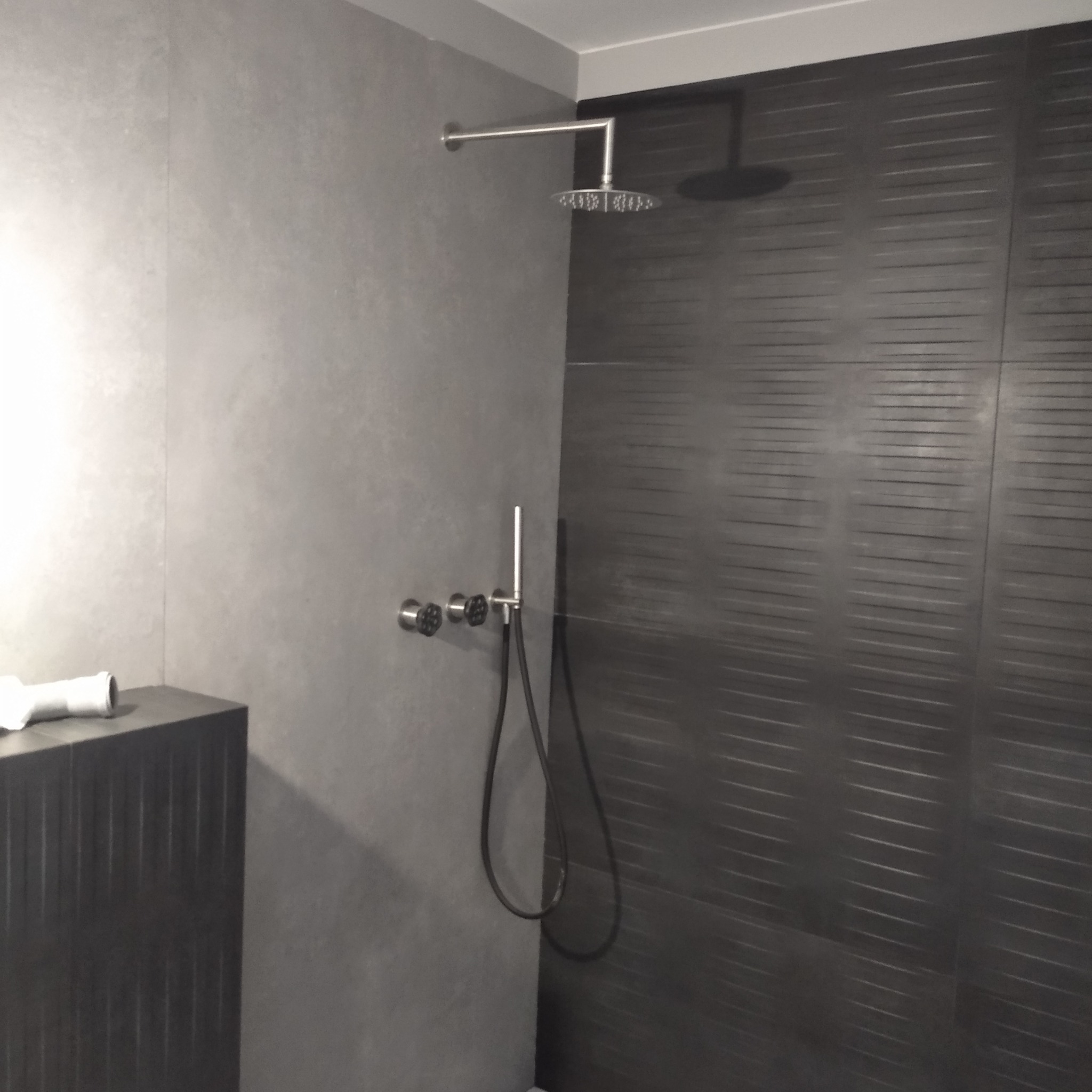 Nowoczesna łazienka z szarą armaturą, deszczownicą i ciemnymi płytkami z poziomymi paskami, minimalistyczny design.