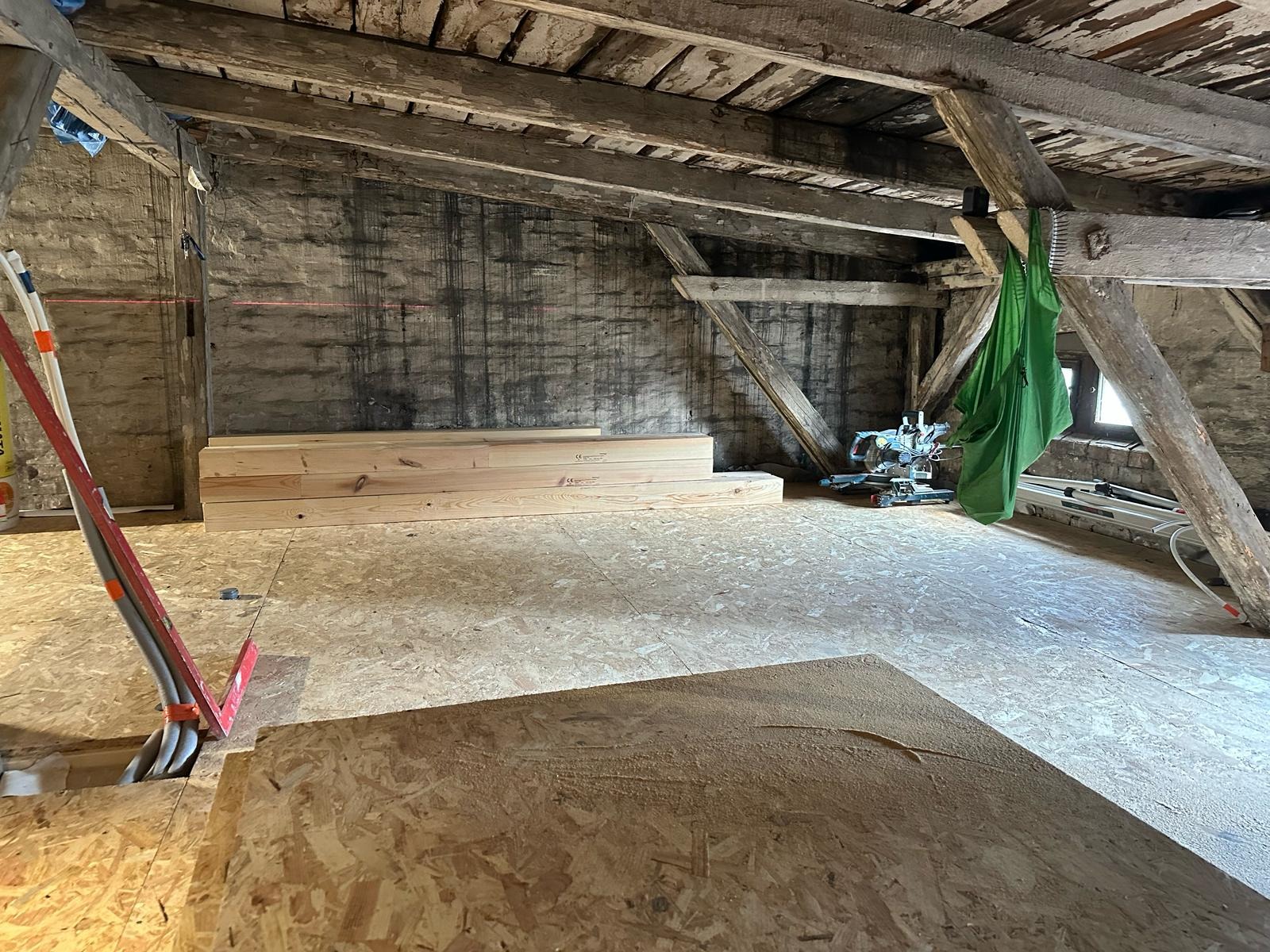 Adaptacja poddasza: surowe drewno, płyty OSB na podłodze, widoczne krokwie i narzędzia, przygotowane do dalszych prac.