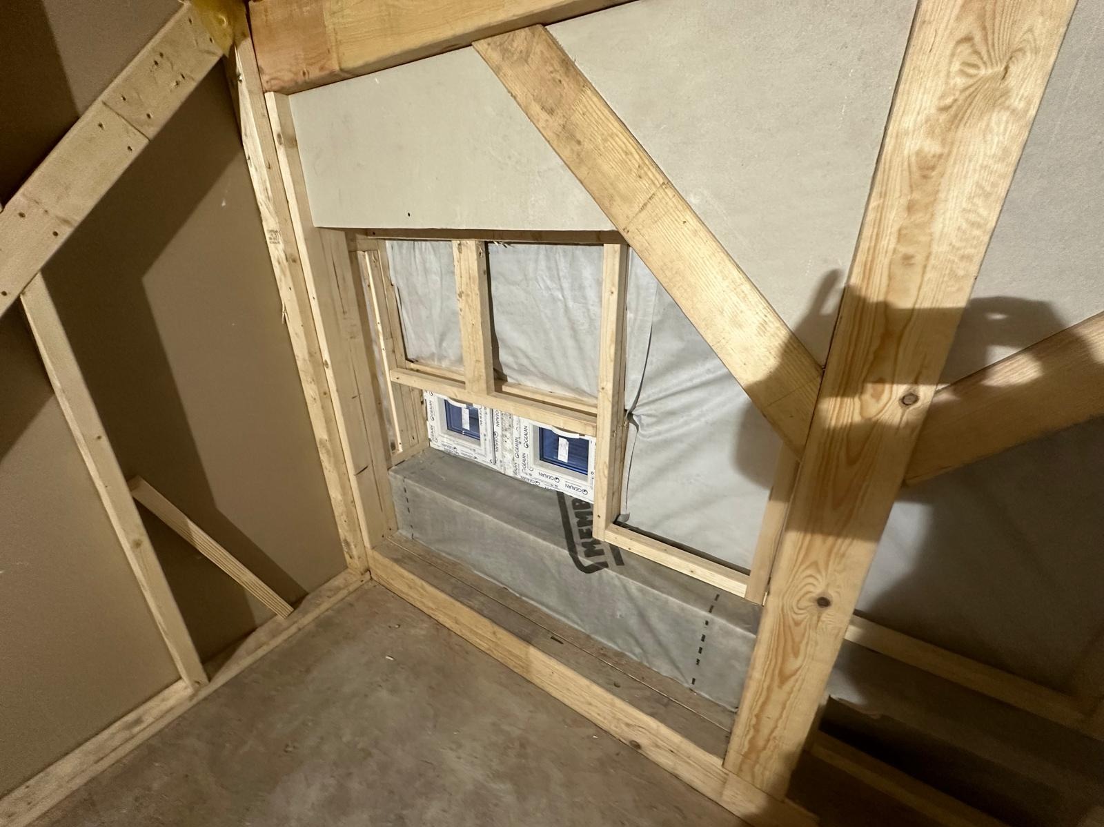 Wnętrze w Gdyni w trakcie budowy domu szkieletowego, widoczne drewniane elementy konstrukcyjne, okno z folią ochronną i fragment ściany z płyt kartonowo-gipsowych.