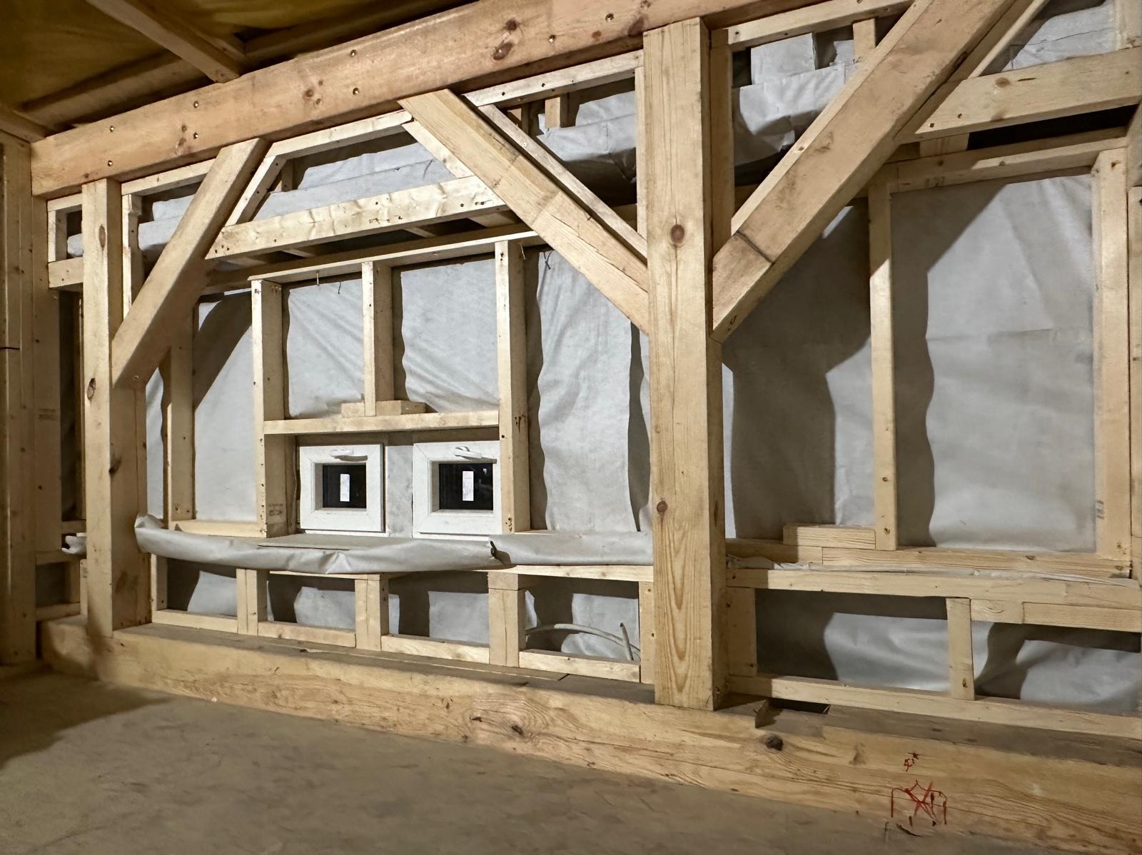 Wnętrze domu w trakcie budowy, widoczna drewniana konstrukcja szkieletowa ścian z oknami, zabezpieczona folią paroizolacyjną.