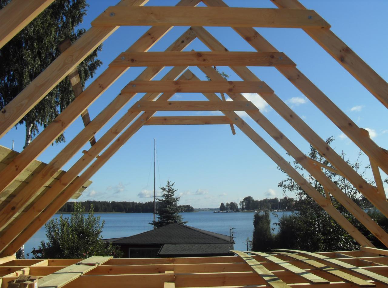 Konstrukcja drewniana dachu z widokiem na jezioro i las. Elementy połączone metalowymi płytkami. W tle błękitne niebo i woda.